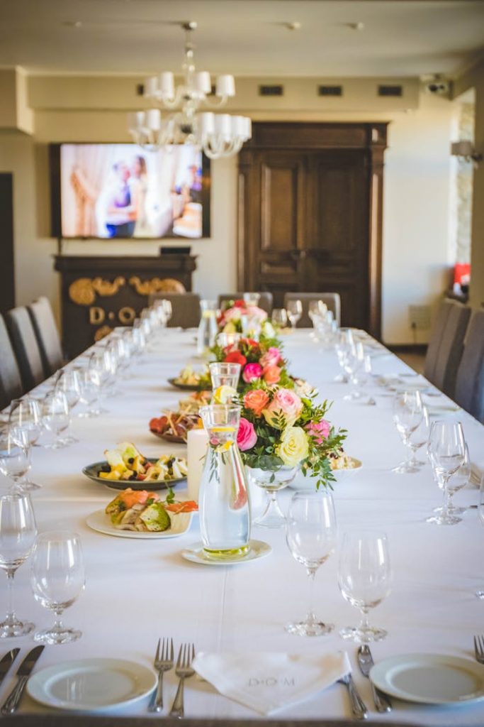 empty-clear-wine-glass-lot-on-table-1123248 Long elegant dining table with a floral centerpiece and tableware set for a formal meal.
