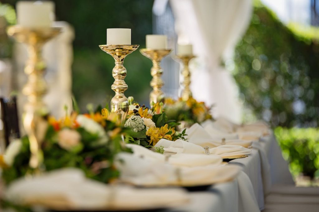 four-white-tealight-candles-on-brass-colored-candlesticks-1128782 Luxurious outdoor wedding table decor with golden candlesticks and vibrant flower arrangements.